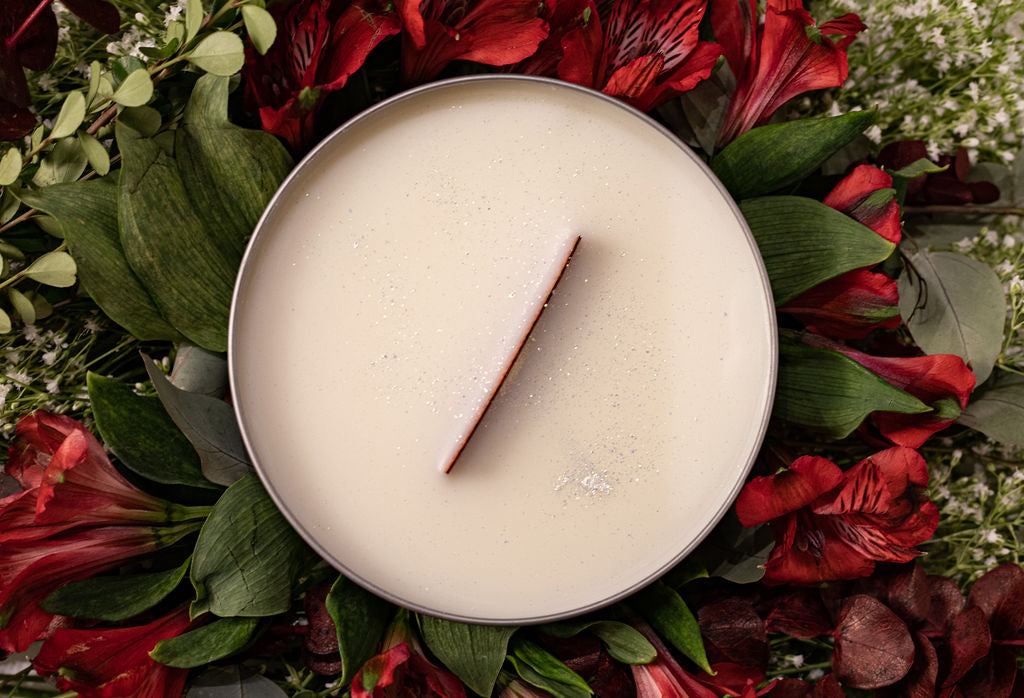 wooden wick candle in a round silver tin surrounded by flowers